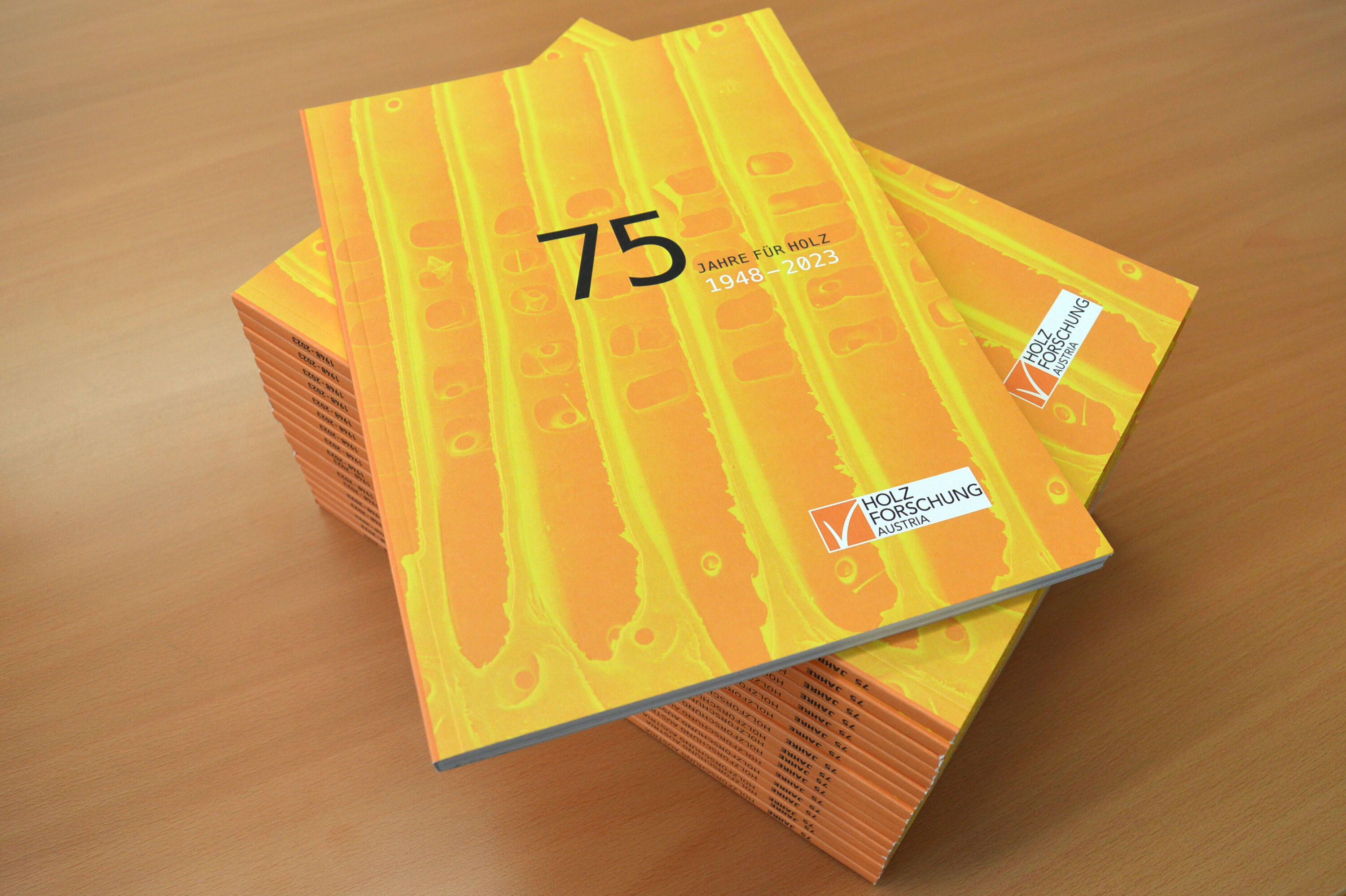 A stack of the commemorative publication marking 75 years of Holzforschung Austria lies on a wooden table.