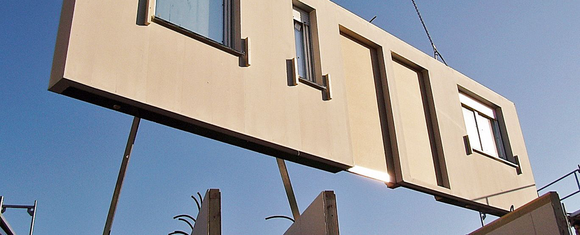 Prefabricated wall element is installed by crane. The sky can be seen in the background.