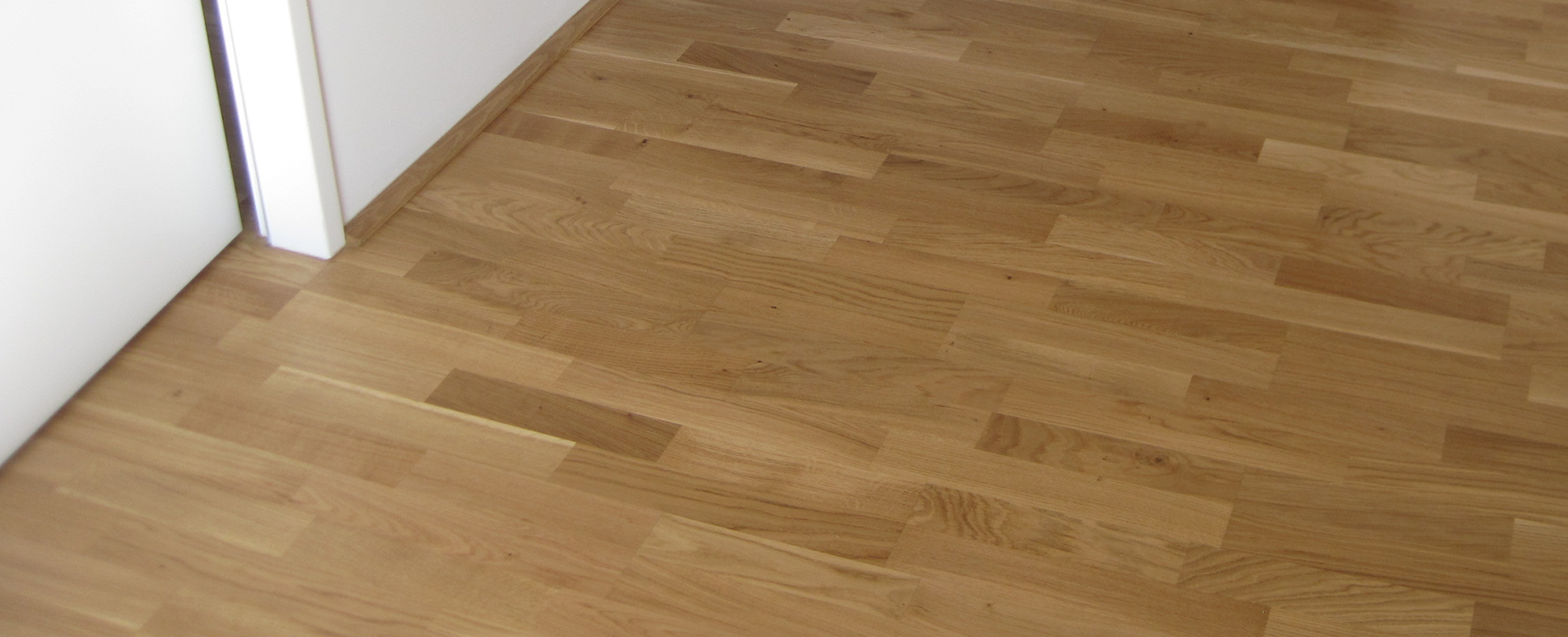 Wooden floor bordering a white wall.