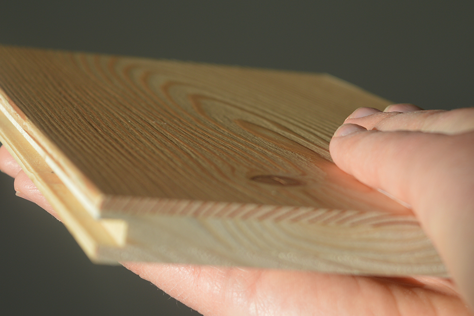 A hand strokes a wooden plank to feel the surface structure.
