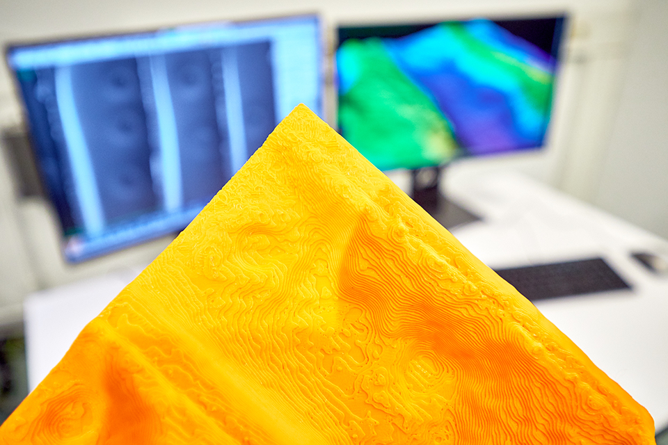 3D-Druck gefertigte, mikroskopische Vergrößerung einer Holzoberfläche in Orange zu sehen.