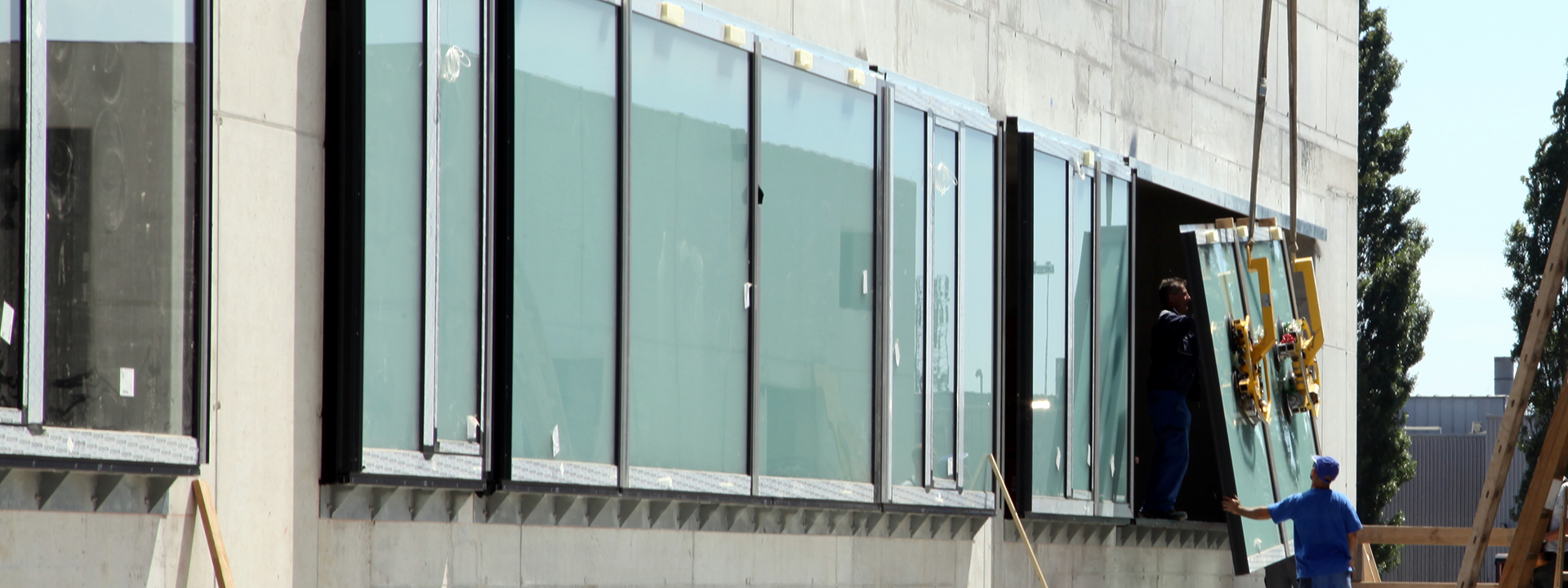 In der Fensterfront eines Betonrohbaues wird ein Fenster mit einem Kran eingesetzt.