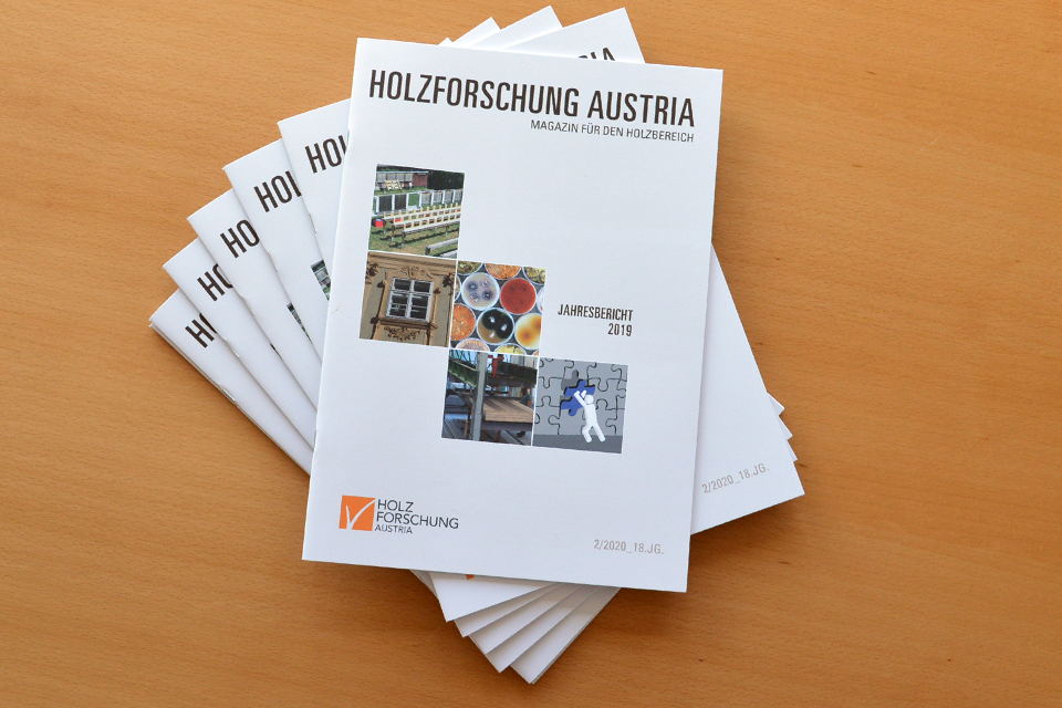 Ein aufgefächerter Stapel Jahresberichte der Holzforschung Austria liegt auf einem Holztisch.