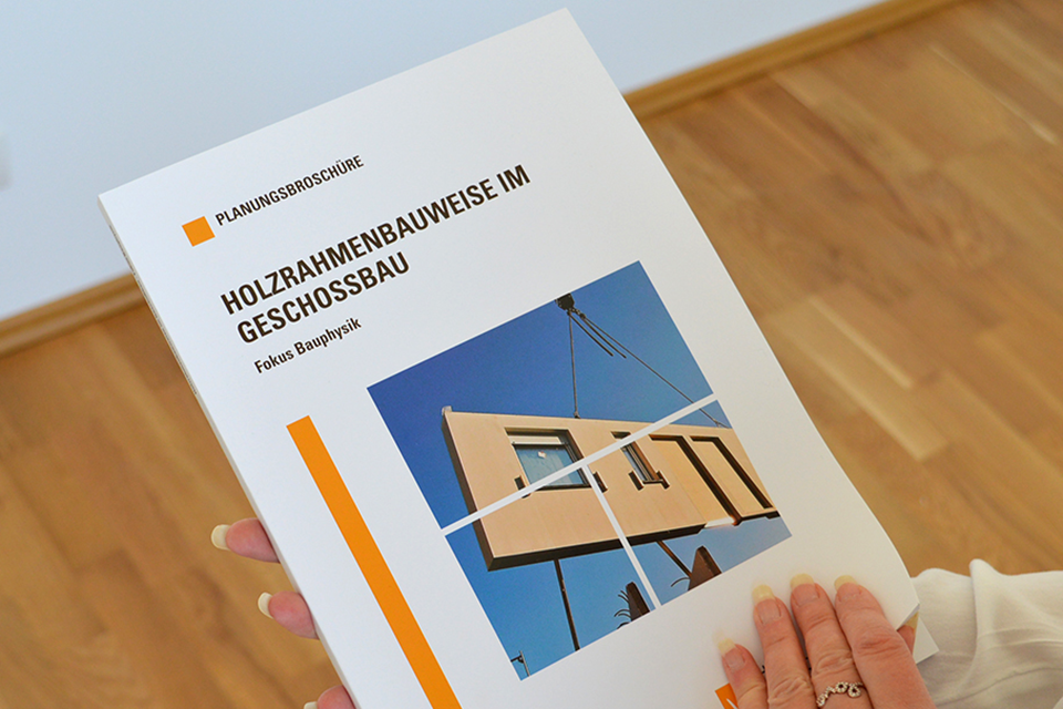 Die Fachbroschüre Bauen mit Brettsperrholz wird von einer Kundin durchgeblättert.